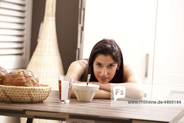 Junge Frau sitzt gemütlich am Esstisch und frühstückt