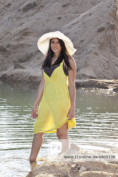 Junge Frau mit Strohhut am Strand eines Baggersees