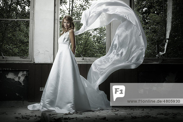 Junge blonde Frau in einem Hochzeitskleid mit wehendem Schleier in einer urbanen Location