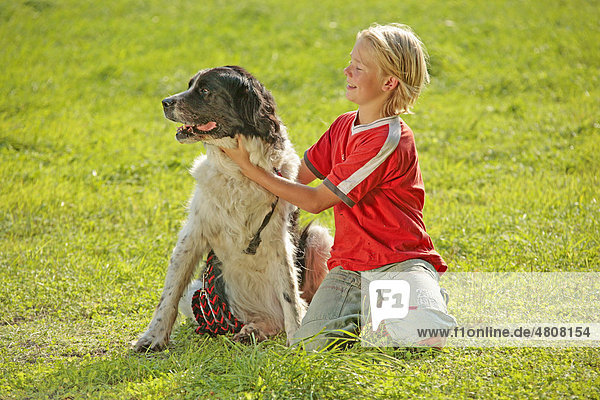 Ein Junge kuschelt mit seinem Hund auf einer Wiese