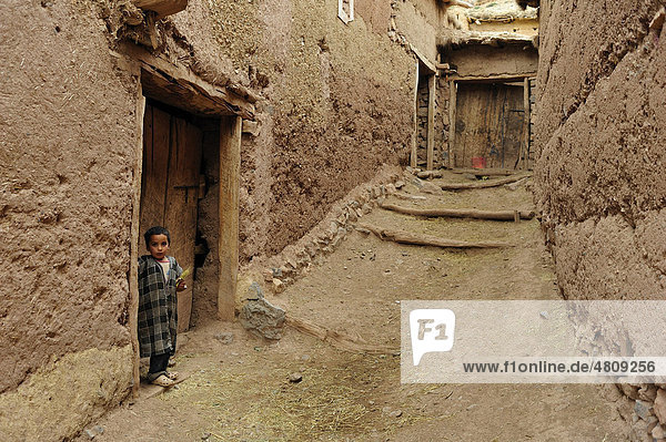 Ein kleiner Berberjunge steht vor der Haustür in einer schmalen Gasse in einem Lehmdorf  Kelaa M`gouna  Hoher Atlas  Marokko  Afrika