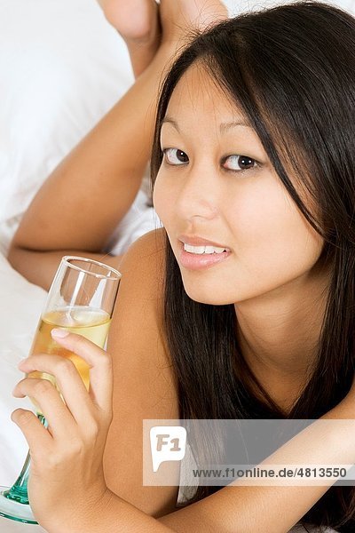Asian woman in early 20´s laying in bed holding a glass of white wine