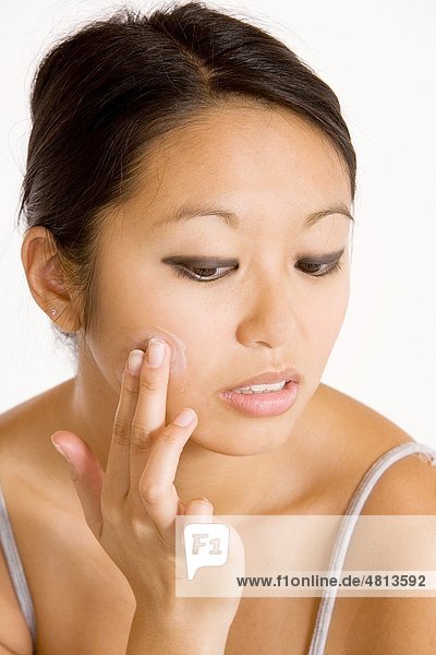 Young Asian woman applying moisturizing cream on her face