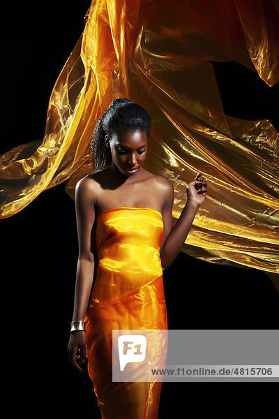 Junge dunkelhäutige Frau in einem goldfarbenen Organzakleid mit wehender Schleppe