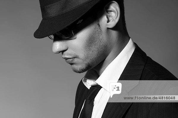Side portrait of a young man with glasses  suit  shirt  tie and hat