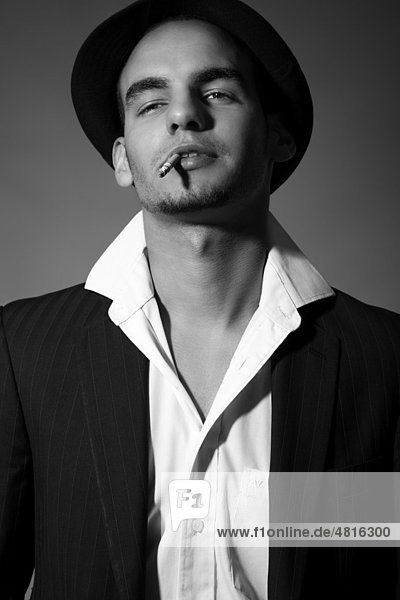 Young man in suit  shirt  tie and hat  with a cigarette in his mouth and a cool look