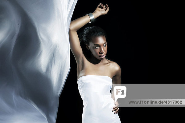 Junge dunkelhäutige Frau in einem weißen Seidenkleid mit wehender Schleppe