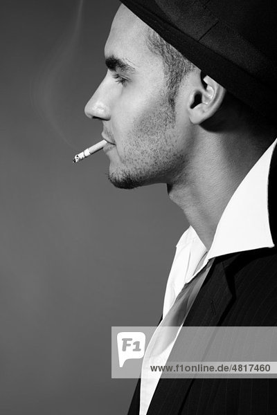 Side profile of a young man wearing a suit  a shirt and a hat with a cigarette in his mouth