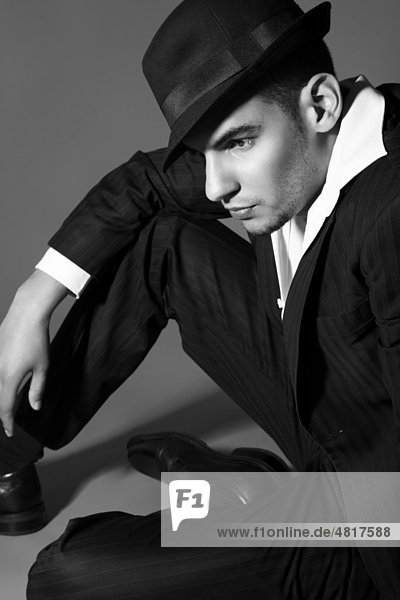 Young man wearing a suit  a shirt and a hat  seated on the ground  lost in thought