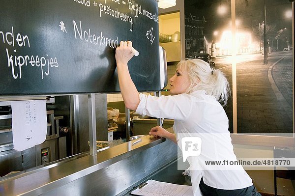 A young adult  blonde waitress is writing the menu of the day to the blackboard of restaurant Wester Paviljoen  prior te receiving guests for diner. Rotterdam  Netherlands
