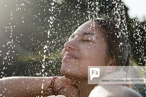 Junge Frau steht unter einer Dusche im Garten