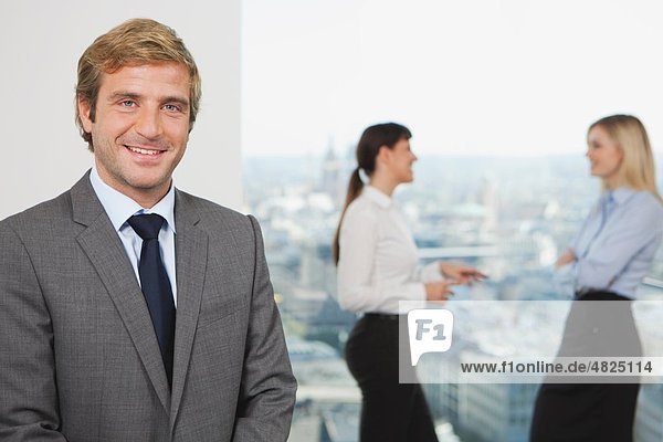 Business man smiling with business people talking in background