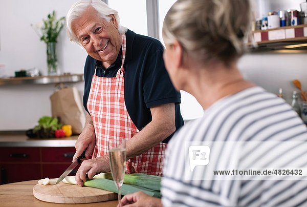 Senior man cutting vegetables with woman in foreground