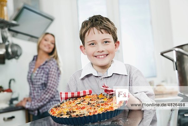 Boy holding pizza with mother in background