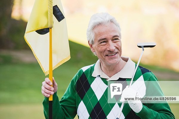 Italien  Kastelruth  reifer Mann mit Golfschläger und Golfflagge  lächelnd