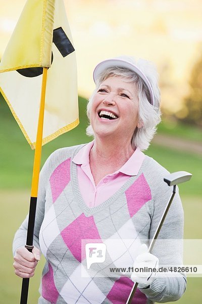 Italien  Kastelruth  Reife Frau mit Golfschläger und Golfflagge auf dem Golfplatz  lächelnd