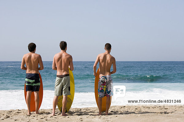 Drei junge Männer am Strand mit Surfbrettern