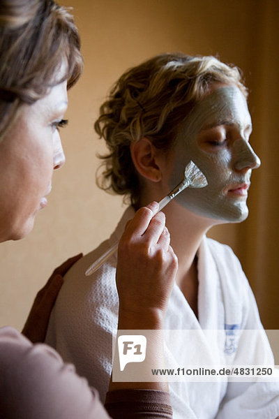 Young woman having mud mask applied to face