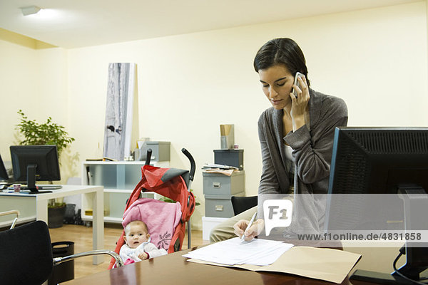 Woman working in office with baby in stroller nearby