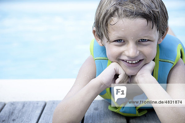 Boy in life jacket leaning against side of pool  portrait