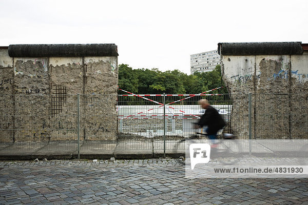 Deutschland  Berlin  Person  die an einem abgebauten Teil der Berliner Mauer vorbeifährt.
