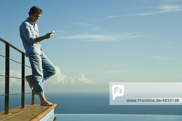 Man standing beside infinity pool  text messaging with cell phone