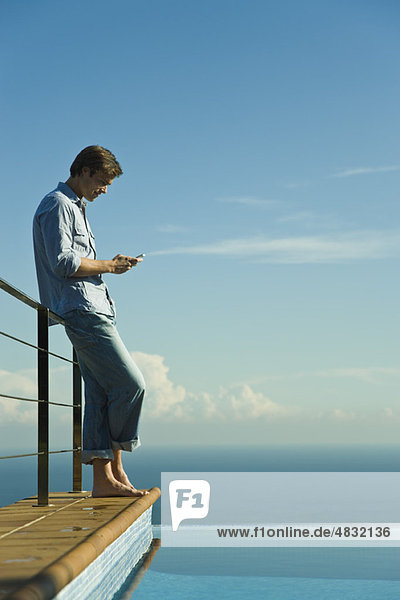 Mann steht neben Infinity-Pool  SMS mit Handy