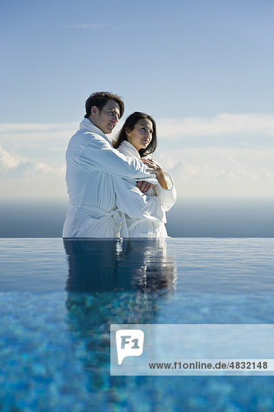 Couple embracing at edge of infinity pool  both wearing bathrobes