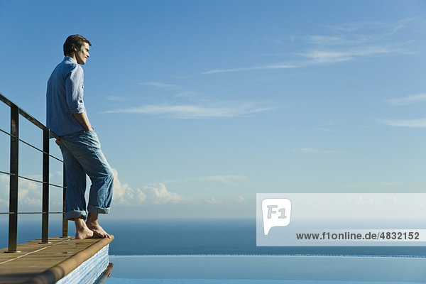 Man standing at edge of infinity pool  looking at view