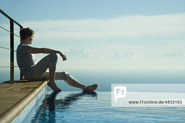 Man sitting on edge of infinity pool  looking at view