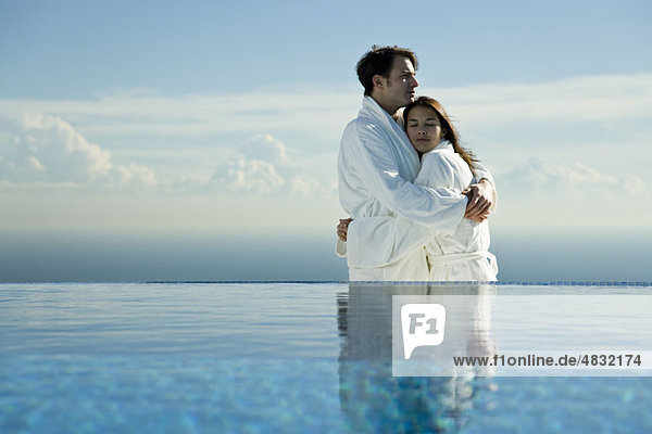 Couple embracing at edge of infinity pool  both wearing bathrobes