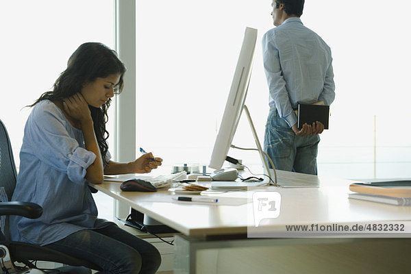Frau arbeitet zu Hause am Schreibtisch  Mann schaut aus dem Fenster im Hintergrund
