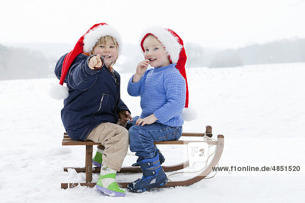 Zwei Jungen auf einem Schlitten mit Weihnachtsmützen