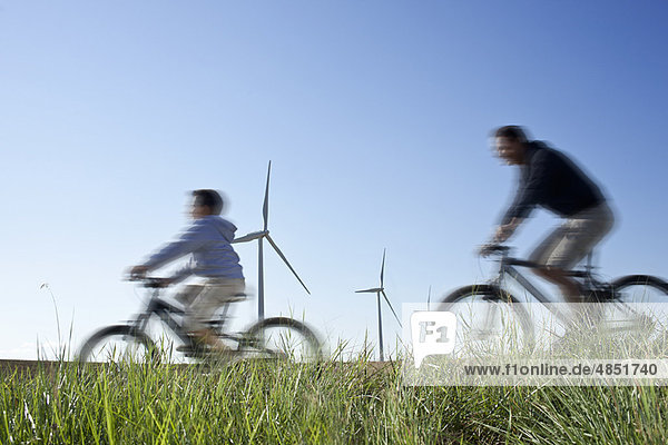 Father and son cycling past a windfarm