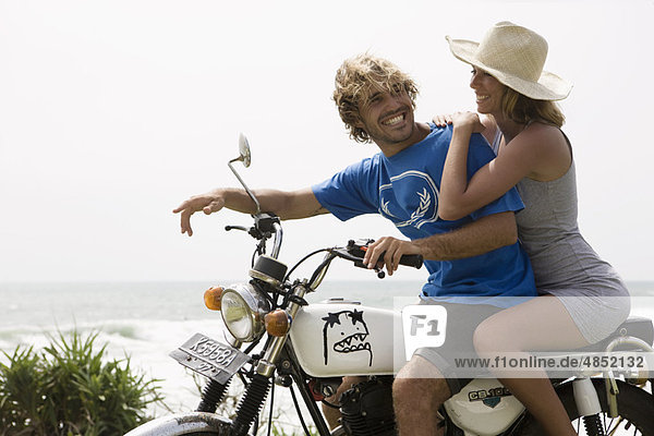 Guy and girl on motorbike laughing  ocean behind them