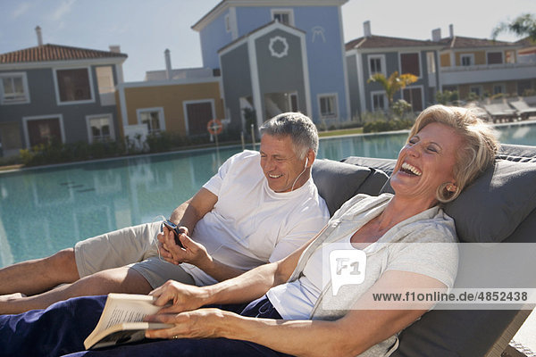 Paar auf Liegen am Pool lachend