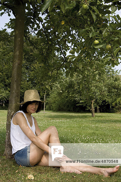 Junge Frau sitzt an einem Apfelbaum
