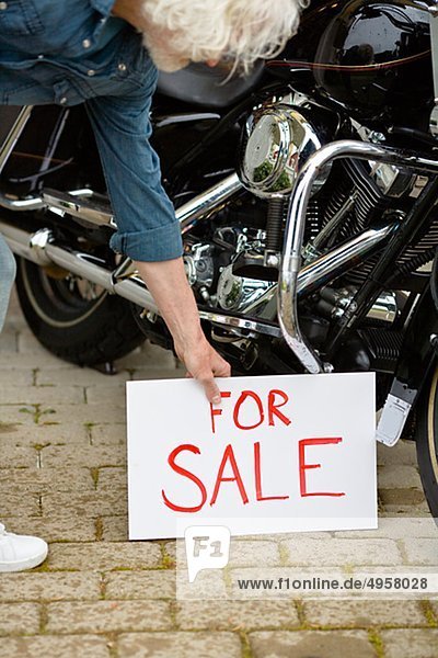 Man putting for sale sign by vintage motorbike
