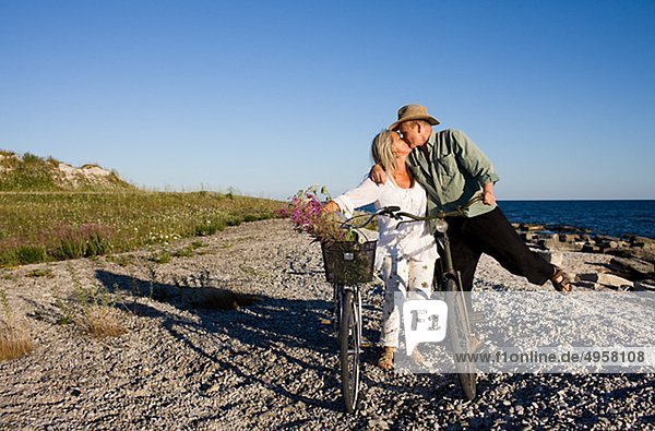reifes Paar Fahrradfahren am Strand und küssen