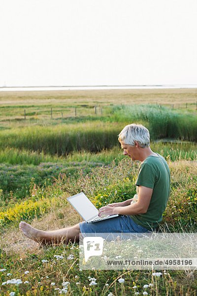 Man sitting on grass using laptop