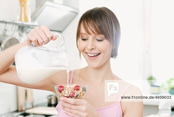 Frau gießt Milch auf Obstmüsli