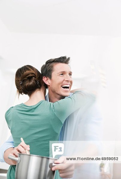 Woman embracing man in kitchen  man prepraring food