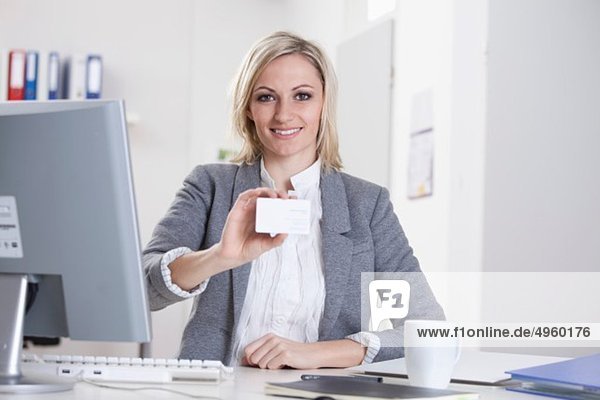 Geschäftsfrau mit leerer Visitenkarte im Büro  lächelnd  Portrait