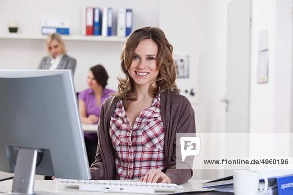 Junge Frau am Computer mit Geschäftsfrauen  die im Hintergrund sprechen