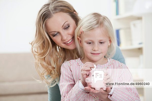 Germany  Bavaria  Munich  Mother and daughter holding piggy bank  smiling