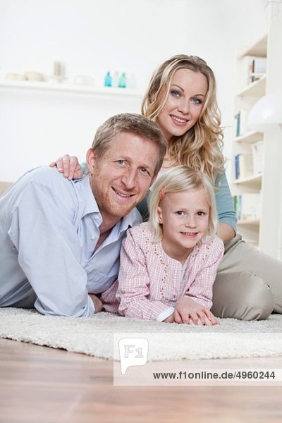 Deutschland  Bayern  München  Eltern mit Tochter auf Teppich liegend  lächelnd  Portrait