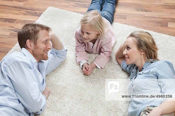 Deutschland  Bayern  München  Eltern mit Tochter auf Teppich liegend  lächelnd