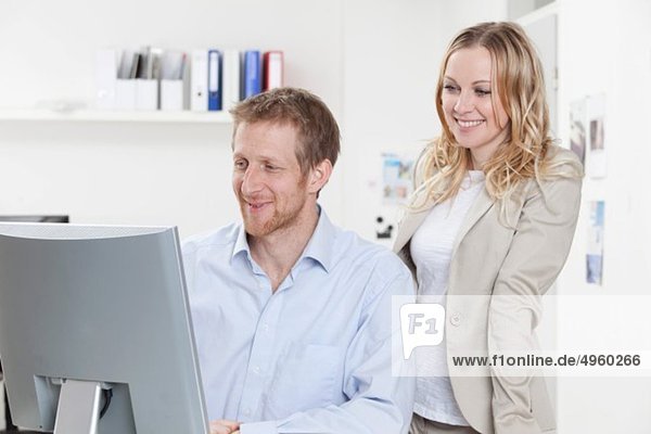 Geschäftsfrau und Geschäftsmann mit Computer im Büro  lächelnd