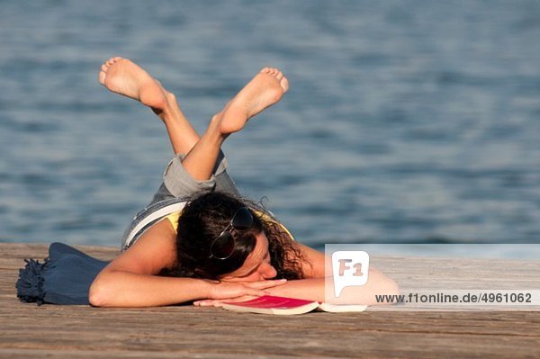 Mid adult woman with book and resting on jetty