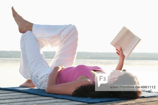 Mid adult woman lying on jetty and reading book